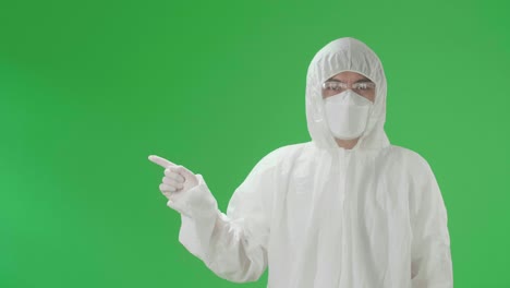 asian man wearing personal protective equipment uniform ppe, medical face mask and pointing to the side in the green screen studio