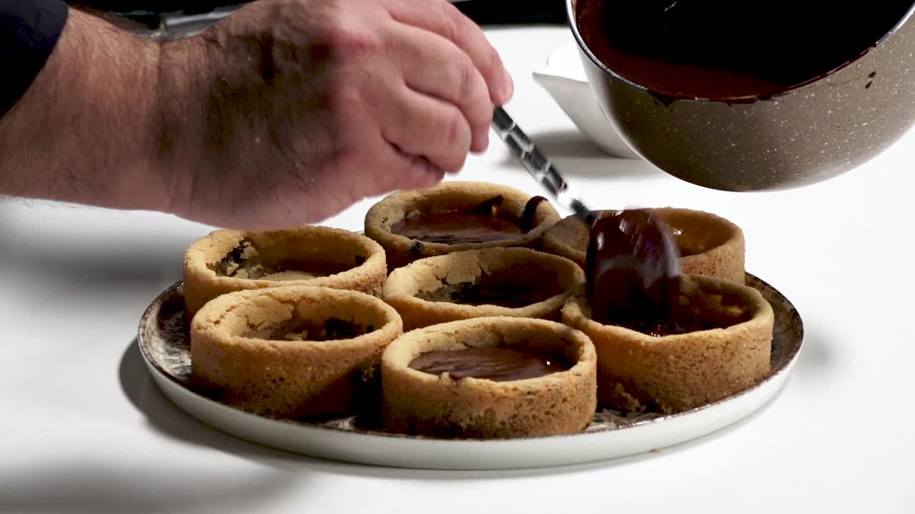 Watch as chocolate filling is carefully spooned into soft cookie cups in a warm kitchen setting, showcasing a delightful dessert creation process