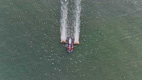 drone topdown shot of a fishers boat dragging the nets thru the water