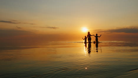 mother with two children laughing in the sea at sunset out of the water