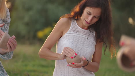 un grupo de mujeres jóvenes crea productos de arcilla usando herramientas para dar forma en un prado en un campo en un parque en un espacio abierto. las chicas hablan sonriendo y discuten el proceso.