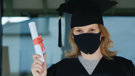 a female graduate in a mask holds a diploma in her hand