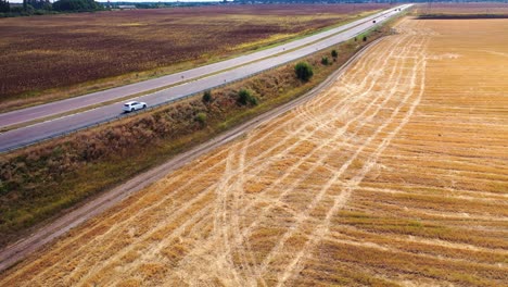 flying over field near the highway. white audi moving slowly on the road on the background of rural landscape. aerial view.