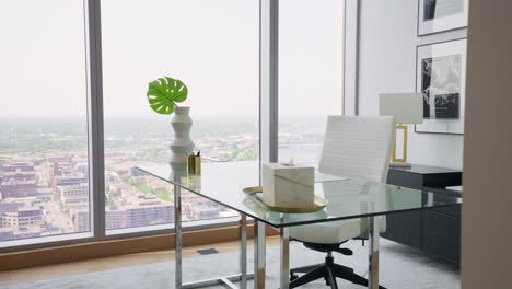 push in shot of a bright office space in a high-rise apartment, featuring large windows that flood the area with abundant natural light with a glass table and a white office chair