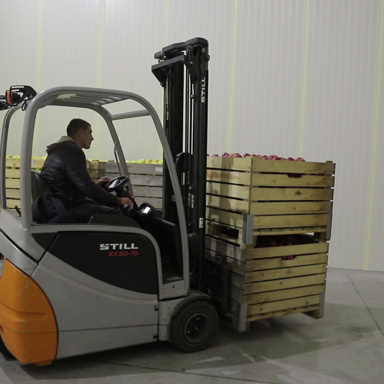 A worker on a loader delivers wooden boxes of ripe apples to the warehouse and places them in rows. Plant for the production of juices.