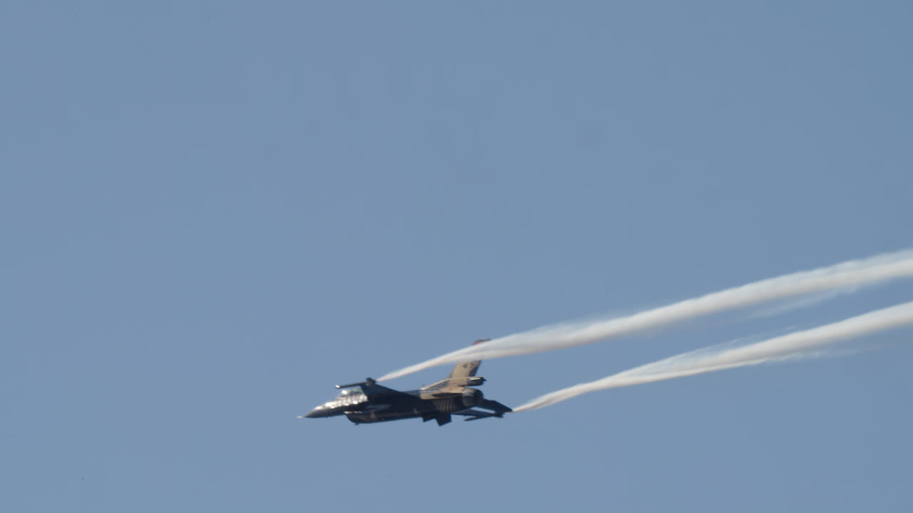 Jet Tempur Terbang dengan Jejak Asap di Langit Biru Cerah