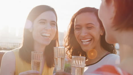 female friends making a toast to celebrate on rooftop terrace with city skyline in background