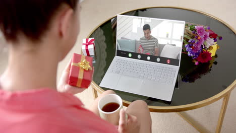 caucasian woman holding red gift using laptop with biracial man on screen