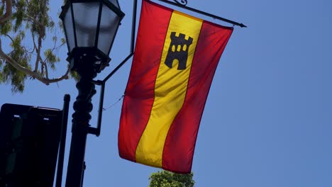 a red and yellow flag with a black castle symbol hangs from a lamppost against a clear blue sky.