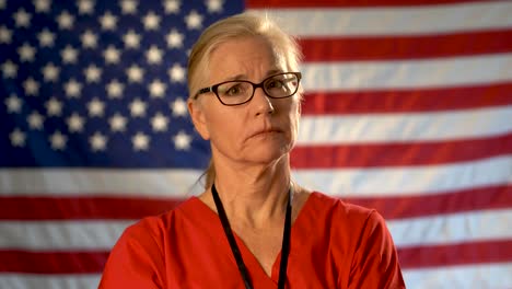 medium tight portrait of a healthcare nurse looking concerned and sympathetic walking towards the camera with an out of focus american flag