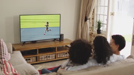 Composite-of-happy-family-sitting-at-home-together-watching-running-athletics-event-on-tv