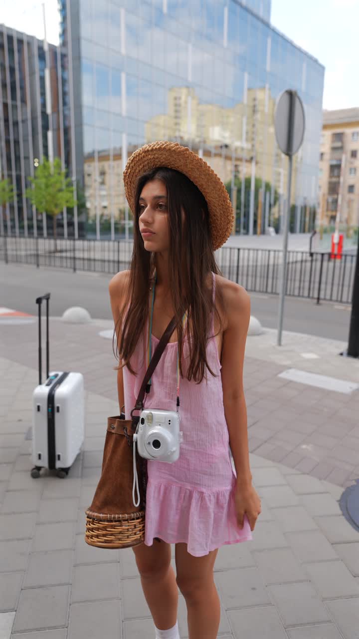 Giovane donna con un vestito rosa e un cappello di paglia in città