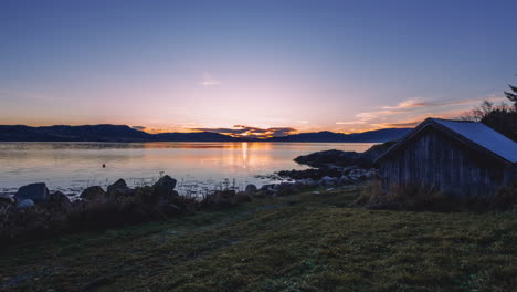 timelapse of a sunset taken from a stony beach with a boat house in trondheim, norway