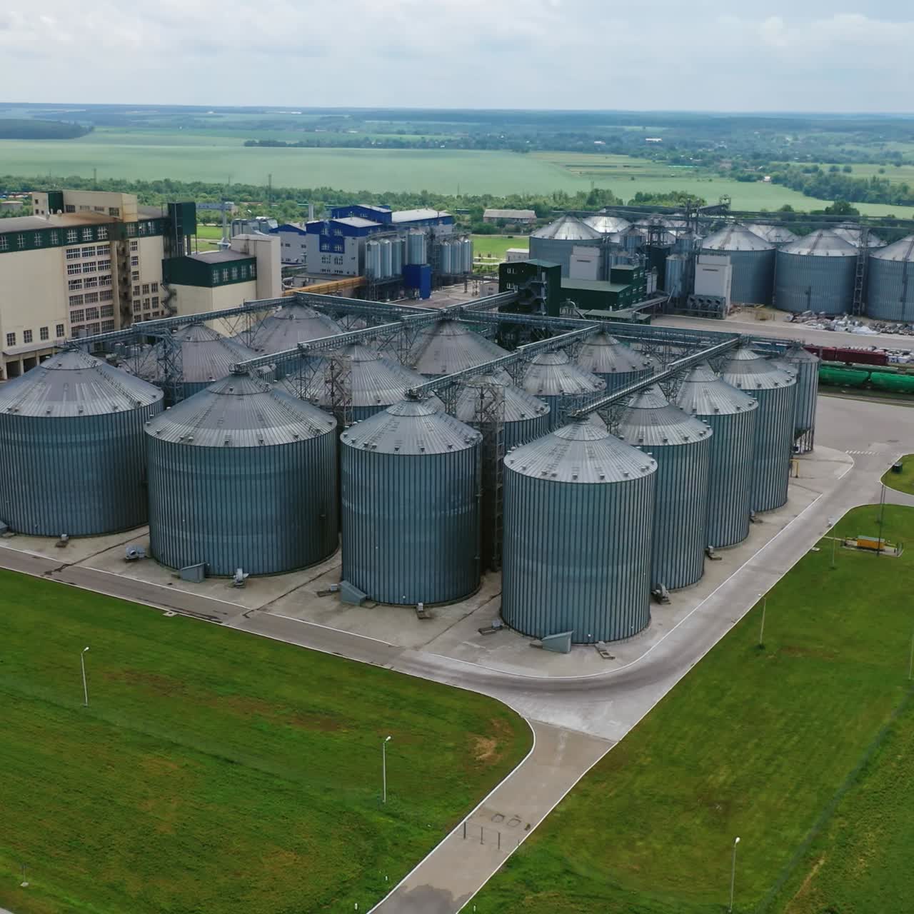 Grain elevator on green landscape. Granary for agricultural crop. Industrial plant with steel containers surrounded by fields. Aerial view.
