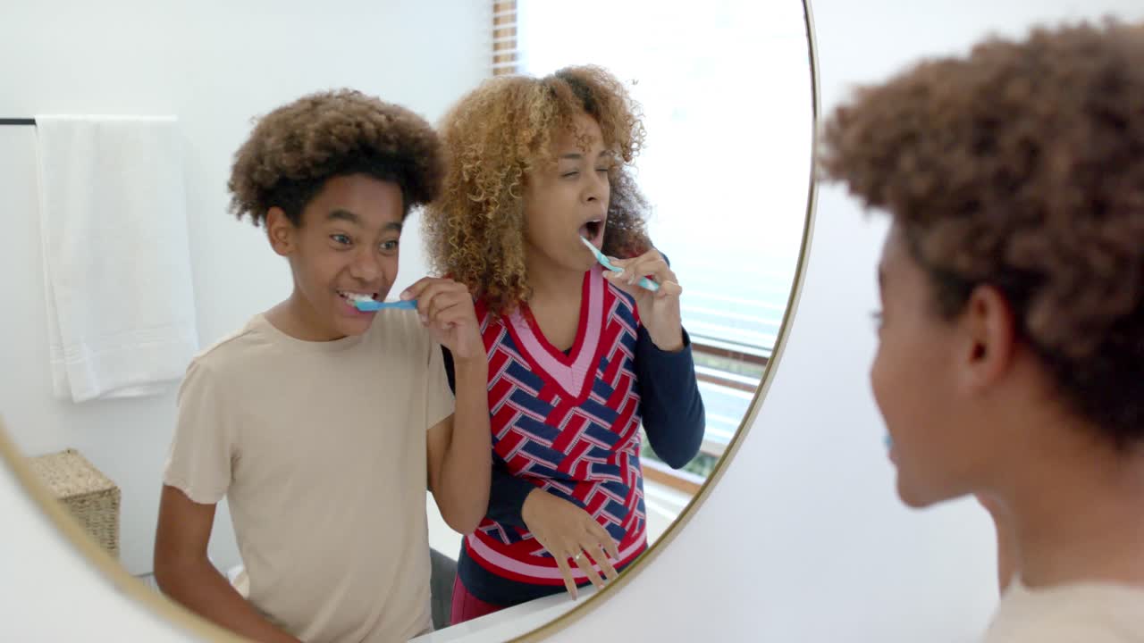 madre y hijo afroamericanos felices cepillándose los dientes en el baño, cámara lenta