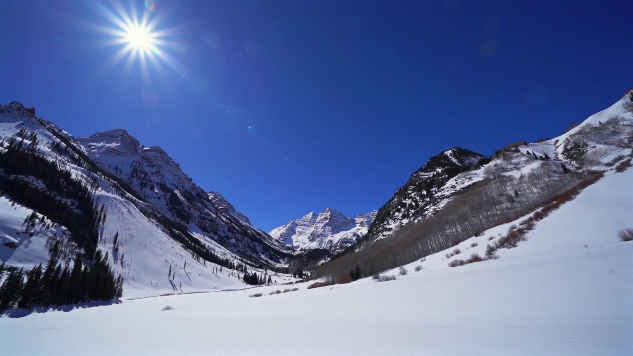 Vinter ved Maroon Lake, Pyramid Peak (14ers) rejser sig over fremtrædende maleriske bjerge, snedækket dal, nøgne aspentræer, morgenens levende solstråler, blå himmel. Maroon Bells, Aspen, Colorado, Rocky Mountains.