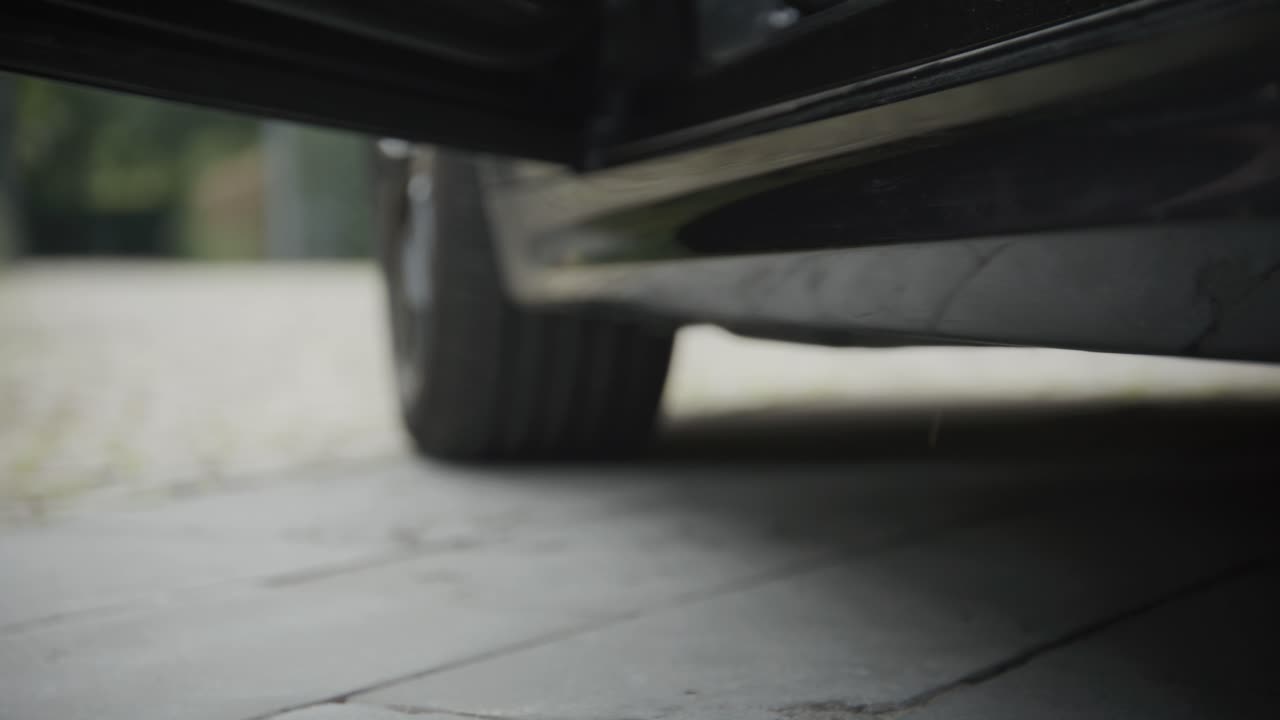Close-up of a car's side and undercarriage on a paved surface, person leaving on high heels, shallow focus