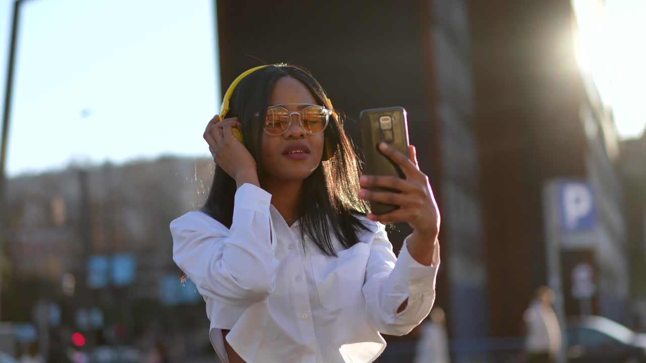 Woman with headphones and sunglasses taking selfie in the city