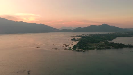 Dreamy-aerial-of-picturesque-and-peaceful-asian-landscape-with-lake,-mountains-and-local-fishing-village-in-Lang-Co,-Vietnam