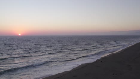 Hermosa-Puesta-De-Sol-Naranja-Y-Rosa-En-Oxnard,-California---Dron-De-4k-Disparado-Lentamente-Hacia-Adelante-Sobre-Las-Olas-Rompiendo-A-Lo-Largo-De-La-Costa