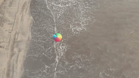 high-drone-shot-Person-walking-on-sandy-beach-under-a-rainbow-umbrella-near-dark-brown-muddy-sea-hope