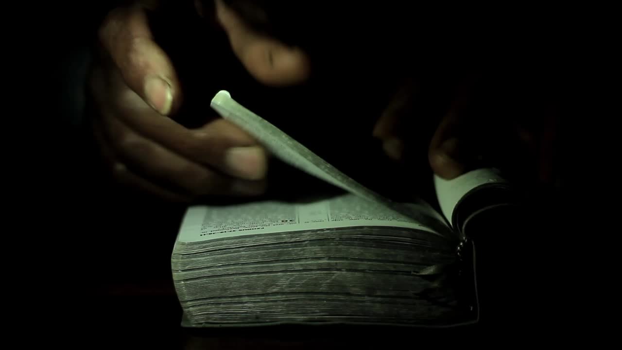 rezando a dios con la mano en el fondo negro de la biblia con la gente metrajes