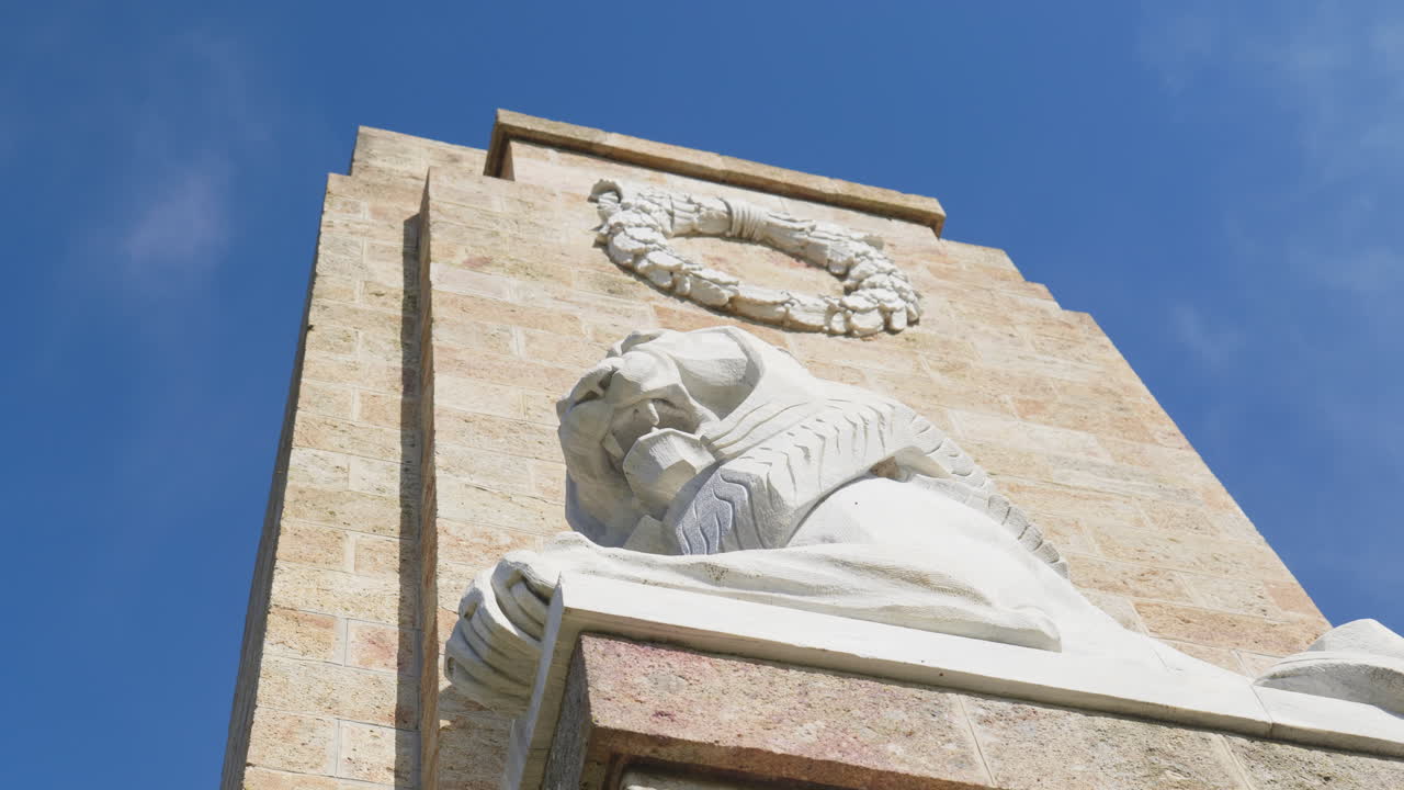 Carrellata dal basso del Memoriale di Doiran, vicino al Lago Doiran, che mostra una statua di leone in marmo e un omaggio floreale sotto cieli azzurri e sereni nella Grecia settentrionale.