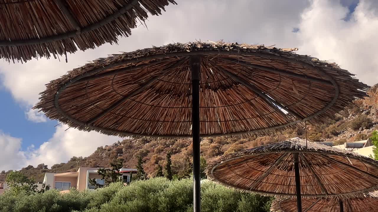 Low angle view of traditional thatched beach umbrellas against a partly cloudy sky in Crete, Greece