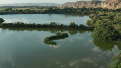 Drohnenaufnahme-Einer-Spanischen-Lagune-Oder-Eines-Sees,-Der-über-Bäume-Mit-Berghintergrund-Fliegt