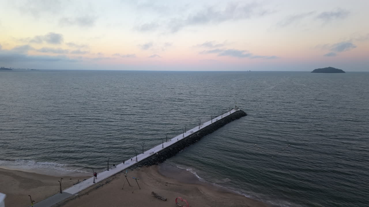 A calm and beautiful aerial shot pushes in towards a long pier at Balneário Piçarras in Santa Catarina, Brazil, capturing the serene seascape and soft colors of the twilight sky over the ocean