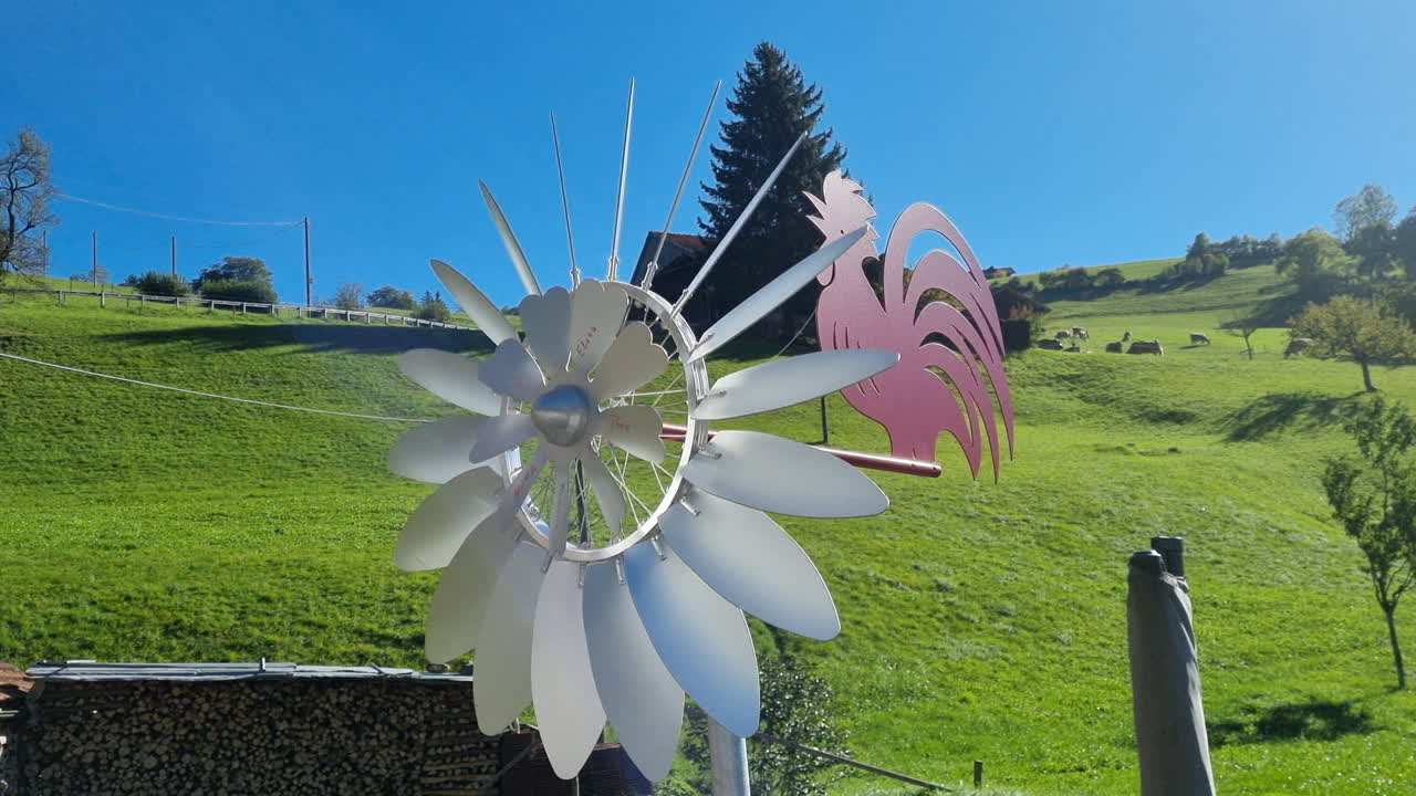 Metal weathercock and pinwheel turning with the wind in front of a green hill in Switzerland