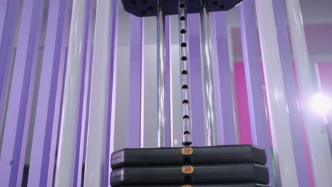 weight stack moving up and down on gym resistance machine, highlighting controlled motion, strength training, and fitness equipment, with purple background