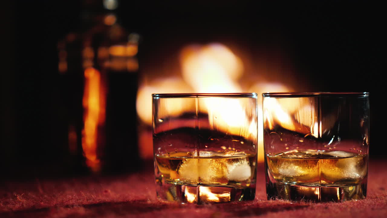 배경에 얼음이 든 위스키 두 잔 병과 불이 타오르는 벽난로