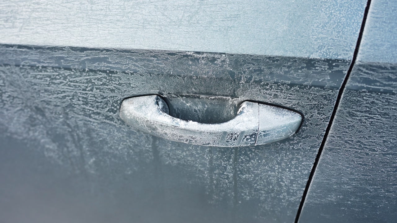 Close-up of a car door handle covered in frost and ice on a cold winter morning, showing frozen vehicle surface texture and deicing or defrosting concept.