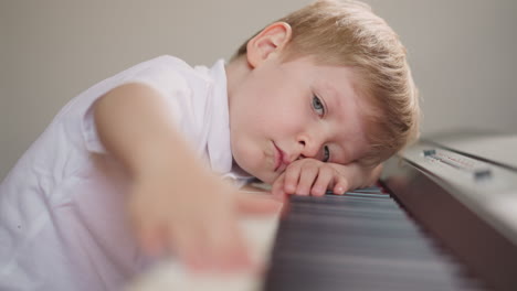 tired boy presses piano keys in row resting head on keyboard