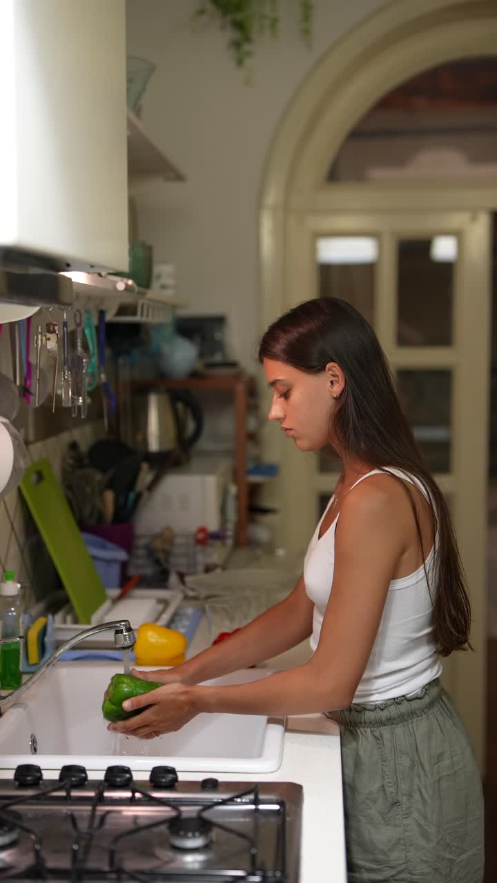 una mujer joven lavando pimientos en una cocina