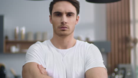 closeup serious man looking camera at home kitchen. focused man crossing hands