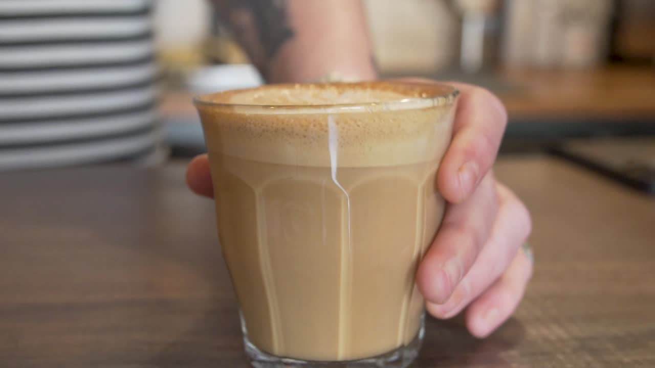 Person Carefully Sets Down Caffe Latte In Table - close up shot