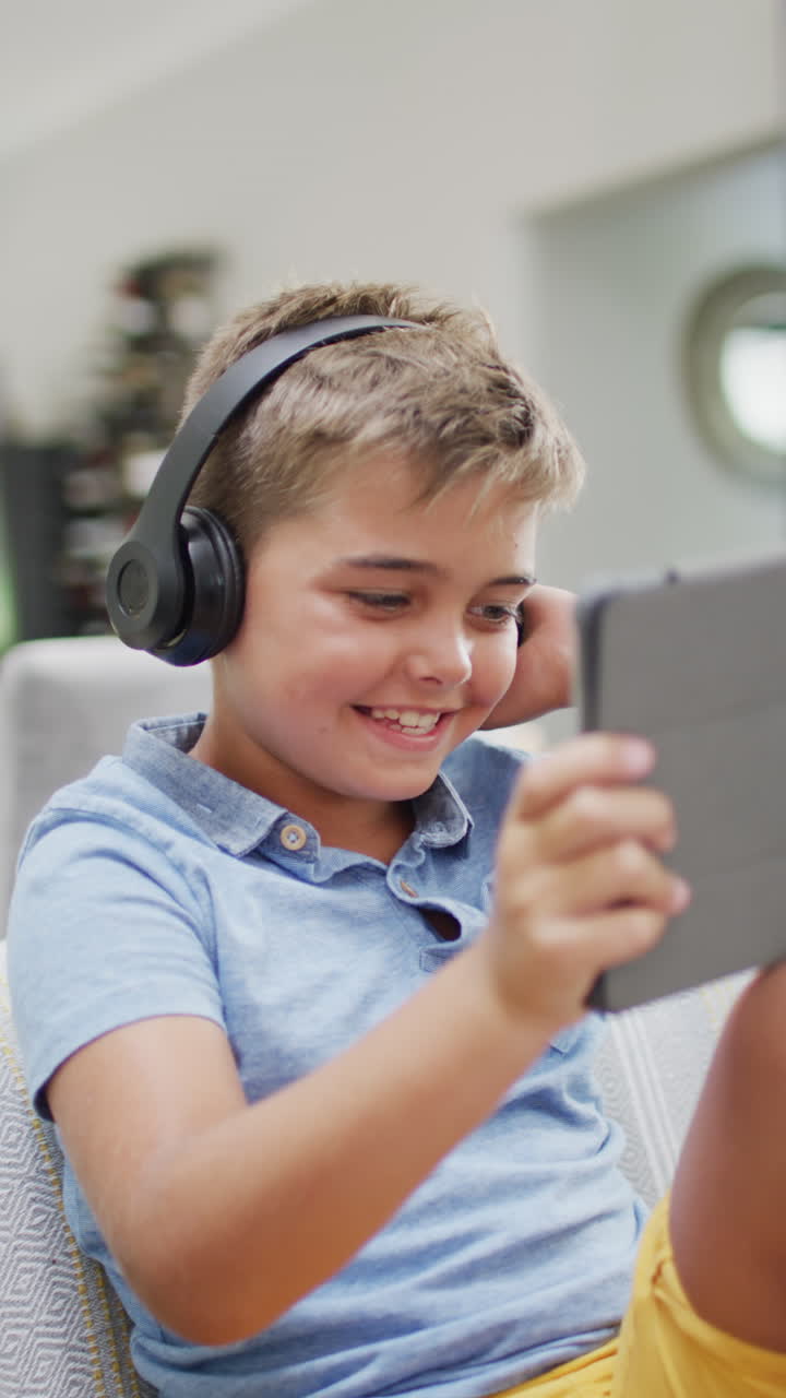 Vertical video of happy caucasian boy lying on sofa and using tablet, slow motion
