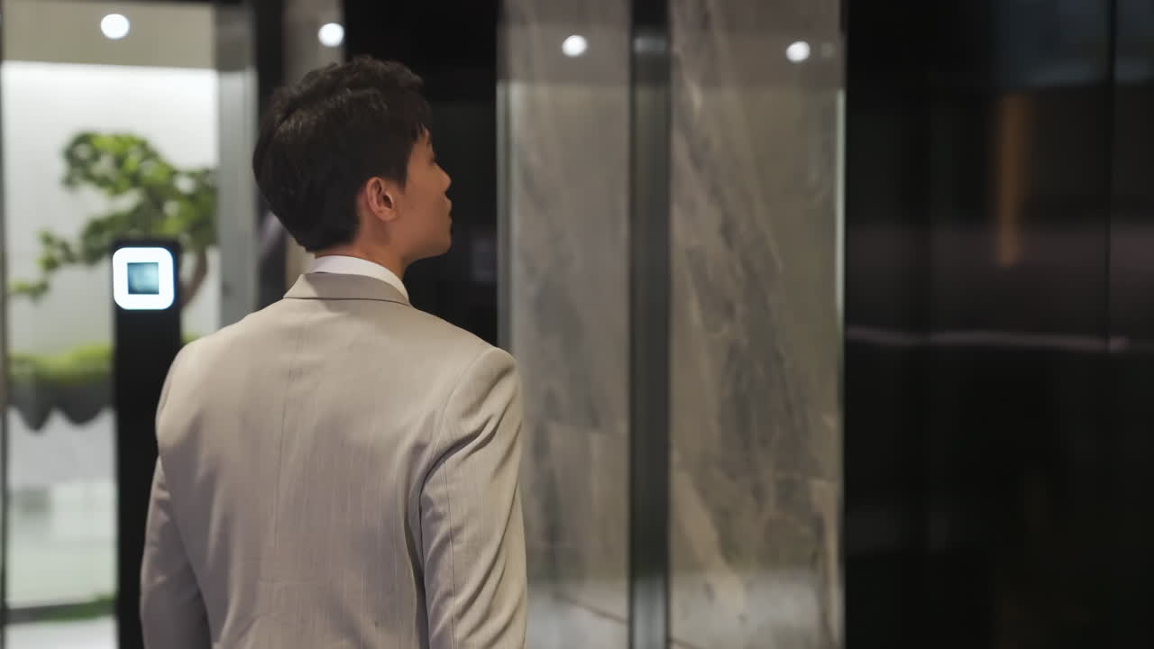 Busy professional businessman in a suit with a briefcase waiting to enter elevator in modern office building during working day, male hand pressing elevator button and looking watch