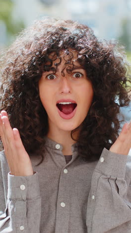 young woman looking surprised at camera shocked by sudden win good victory news, wow in city street