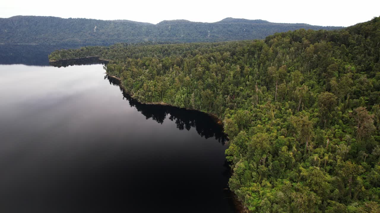 Lake Mapourika With Reflections Bordered By Dense Green Forest And Mountains In Distance. West Coast Of New Zealand's South Island. aerial shot