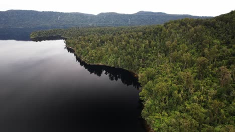lake mapourika with reflections bordered by dense green forest and mountains in distance. west coast of new zealand's south island. aerial shot