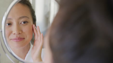 Happy-asian-woman-looking-at-mirror-and-touching-face-in-bathroom,-in-slow-motion