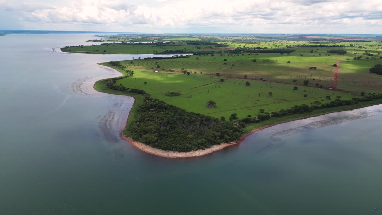 High-angle drone shot of a massive reservoir in Mato Grosso do Sul, Brazil, bordering expansive, well-maintained green farmlands and a small patch of native forest