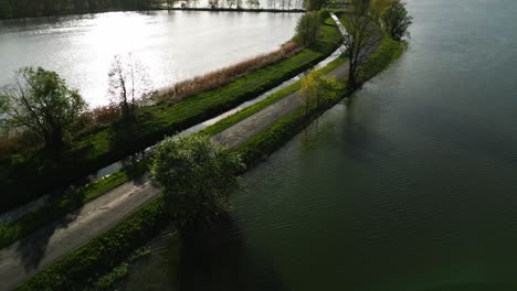 Scenic-drone-footage-captures-a-winding-road-nestled-between-two-lakes,-surrounded-by-lush-greenery-and-reflecting-the-peaceful-beauty-of-nature