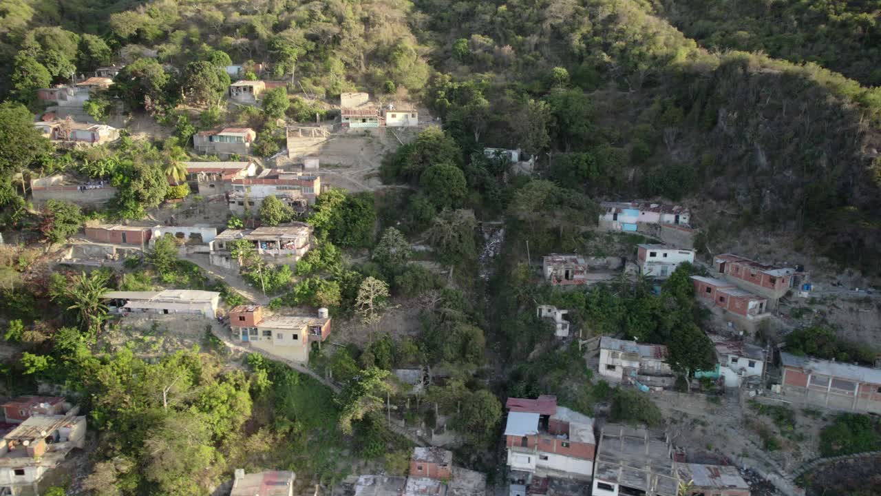 A hillside community with scattered homes, lush greenery, and rugged terrain, looking towards maiquetía, aerial view