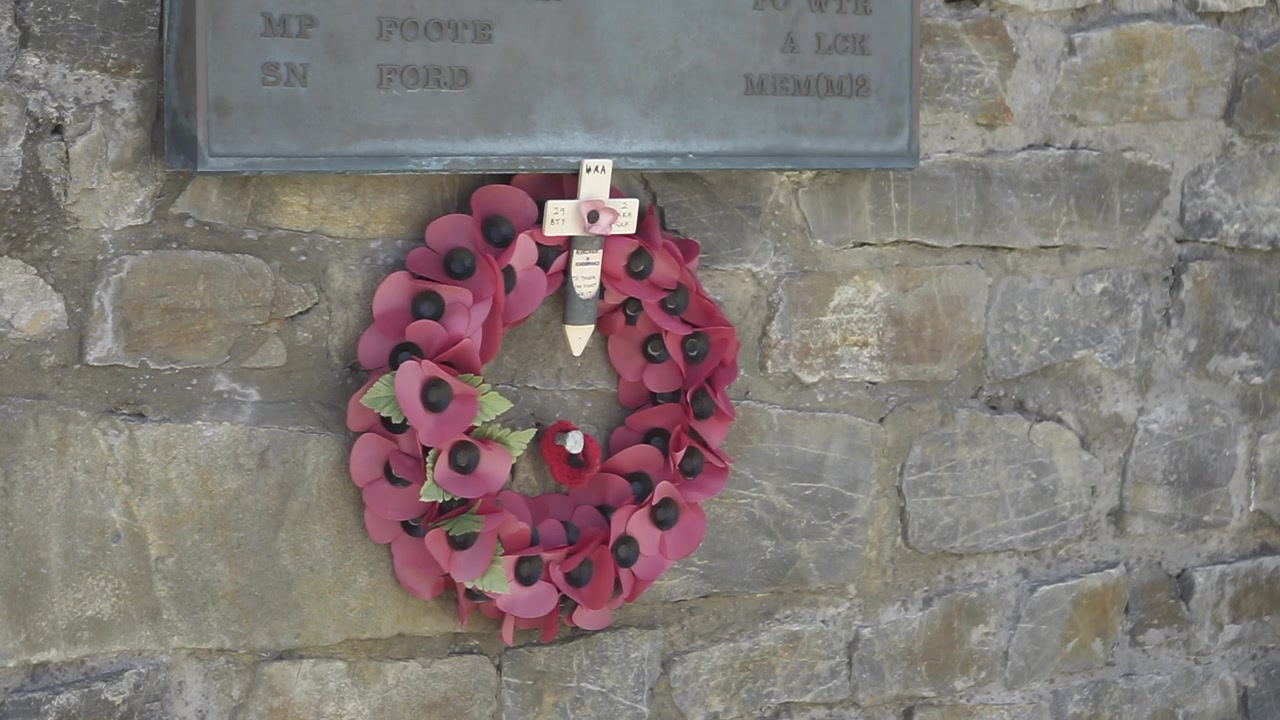 Poppy wreath with a cross hangs on a stone wall, honoring the memory of those lost in war and commemorating their sacrifice