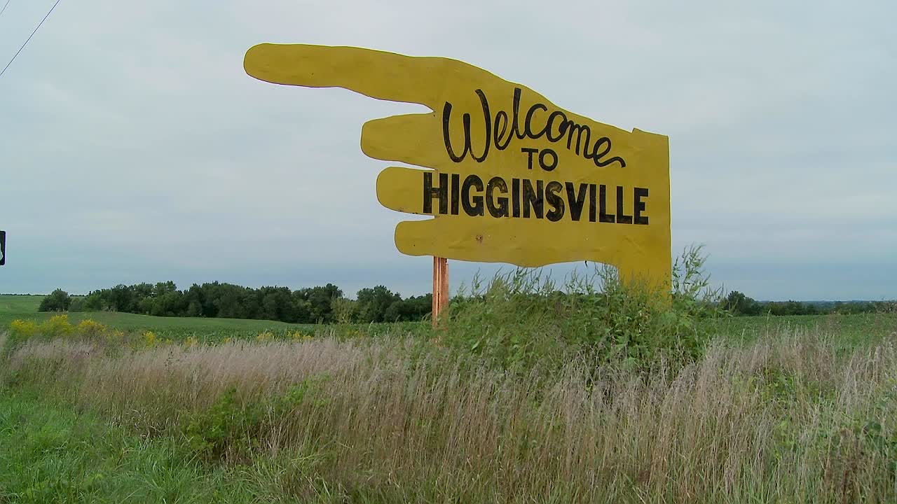 un gran cartel amarillo apunta a higginsville missouri desde un campo agrícola 1