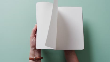 close up of hand leafing through book with copy space on green background in slow motion